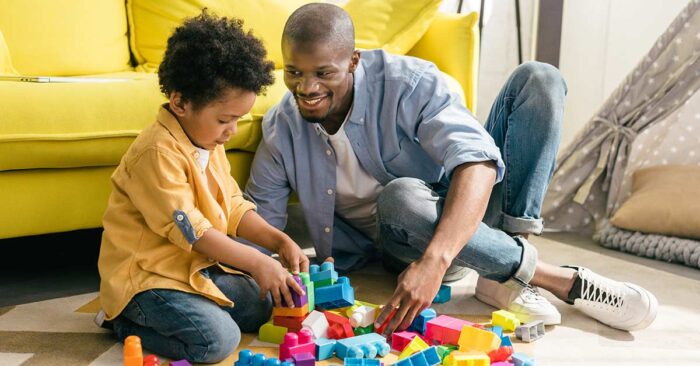 Vater und Sohn sitzen vor gelbem Sofa auf dem Boden und spielen mit Bauklötzen - Scheidungsimmobilie