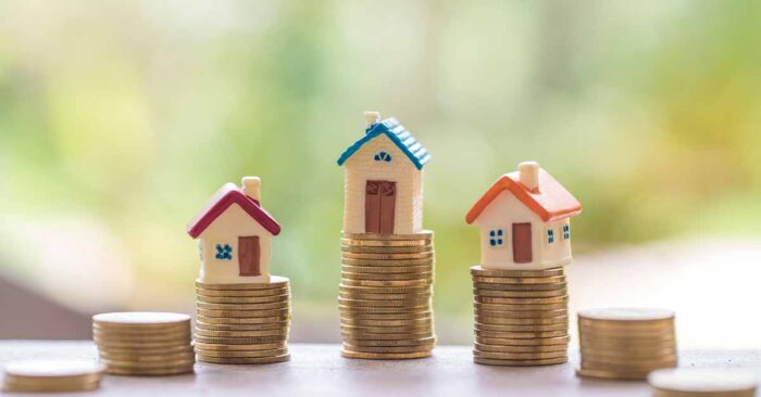 Immobilienfinanzierung Drei Modellhäuschen stehen auf Stapeln von Münzen - Immobilienfinanzierung