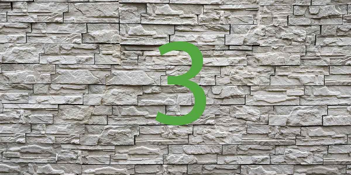 Vor einer Steinmauer steht eine grüne 3 | Haus aus dem 3D-Drucker