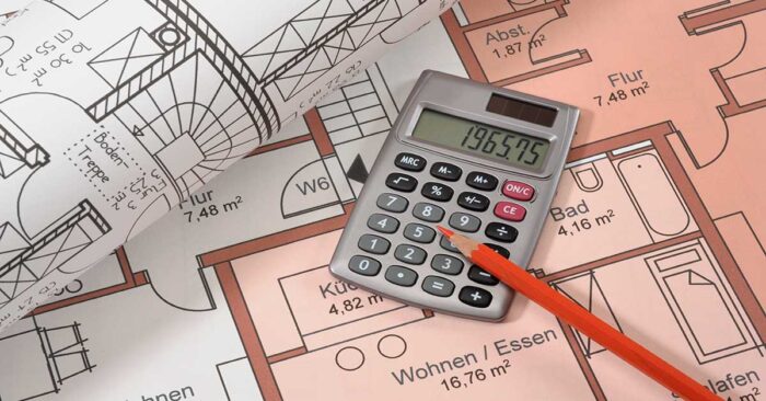 Immobilienfinanzierung Auf dem Grundrissplan einer Immobilie liegen ein weiterer zusammengerollter Grundrissplan, ein Taschenrechner und ein Stift | Immobilienfinanzierung