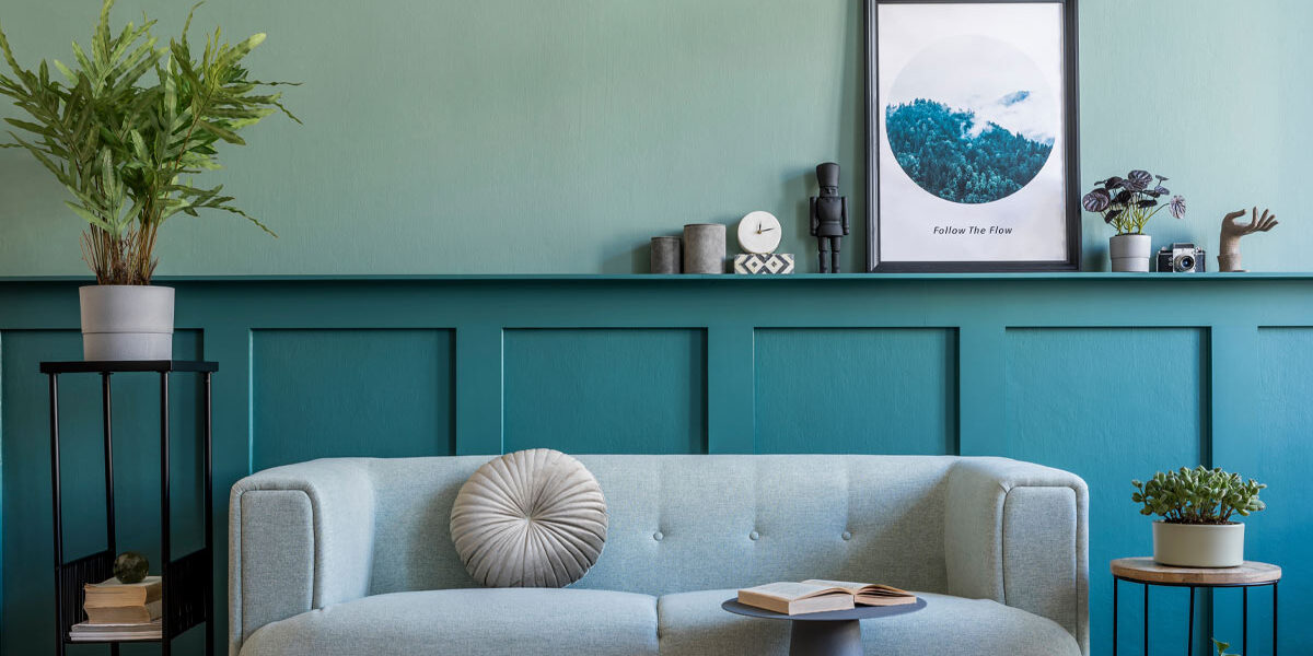 Home Staging Ein mit Home Staging hübsch eingerichtetes Wohnzimmer mit einem eleganten Sofa, mit einem Beistelltisch mit einem Buch, mit Pflanzen rechts und links des Sofas sowie weiteren schlichten Deko-Elementen | Home Staging