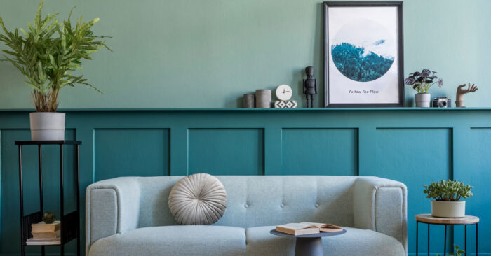 Home Staging Ein mit Home Staging hübsch eingerichtetes Wohnzimmer mit einem eleganten Sofa, mit einem Beistelltisch mit einem Buch, mit Pflanzen rechts und links des Sofas sowie weiteren schlichten Deko-Elementen | Home Staging