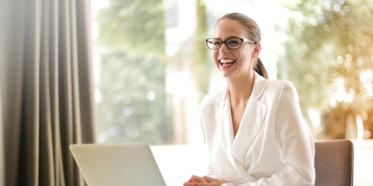 Immobilienbewertung Eine Frau sitzt lachend an ihrem Laptop und freut sich über die gute Online-Bewertung ihrer Immobilie | Immobilienbewertung