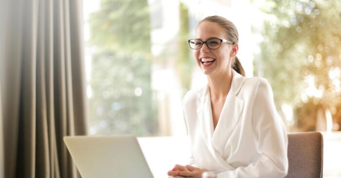 Eine Frau sitzt lachend an ihrem Laptop und freut sich über die gute Online-Bewertung ihrer Immobilie | Immobilienbewertung