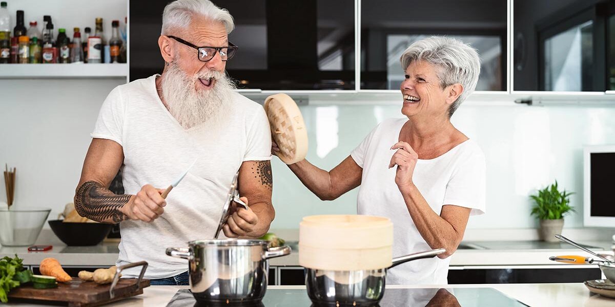 Ein Seniorenpaar steht glücklich in der neuen, kleineren und altersgerechten Wohnung und albert herum | Wohnen im Alter