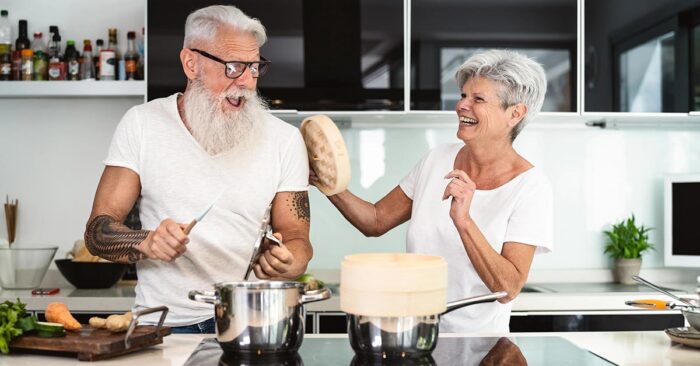 Ein Seniorenpaar steht glücklich in der neuen, kleineren und altersgerechten Wohnung und albert herum | Wohnen im Alter