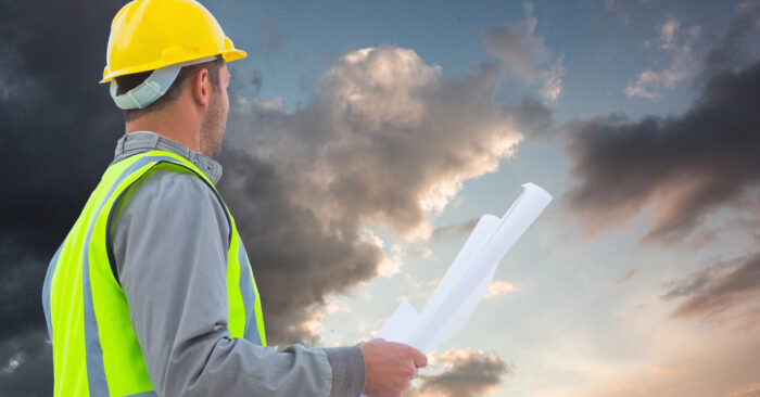 ein Bauarbeiter vor einer Gewitterwand; als symbol für eine Krise im Neubau