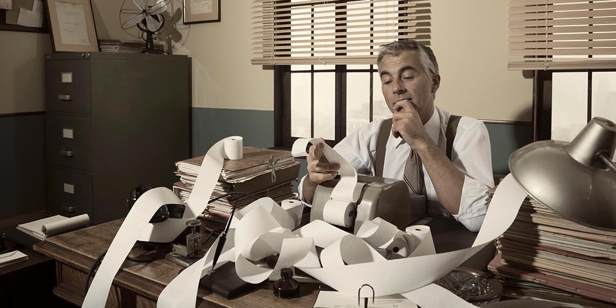 Buchhalter im Büro mit endloser Papierrolle und Rechenmaschine – Symbol für Bürokratie und Steuern | Spekulationssteuer Immobilienverkauf