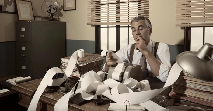 Buchhalter im Büro mit endloser Papierrolle und Rechenmaschine – Symbol für Bürokratie und Steuern | Spekulationssteuer Immobilienverkauf