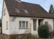 Ein älteres Einfamilienhaus mit verwitterter Fassade und sanierungsbedürftigem Dach steht in einer Wohnstraße und symbolisiert die Entscheidung zwischen Modernisierung und Verkauf. I Sanierungspflicht beim Verkaufen